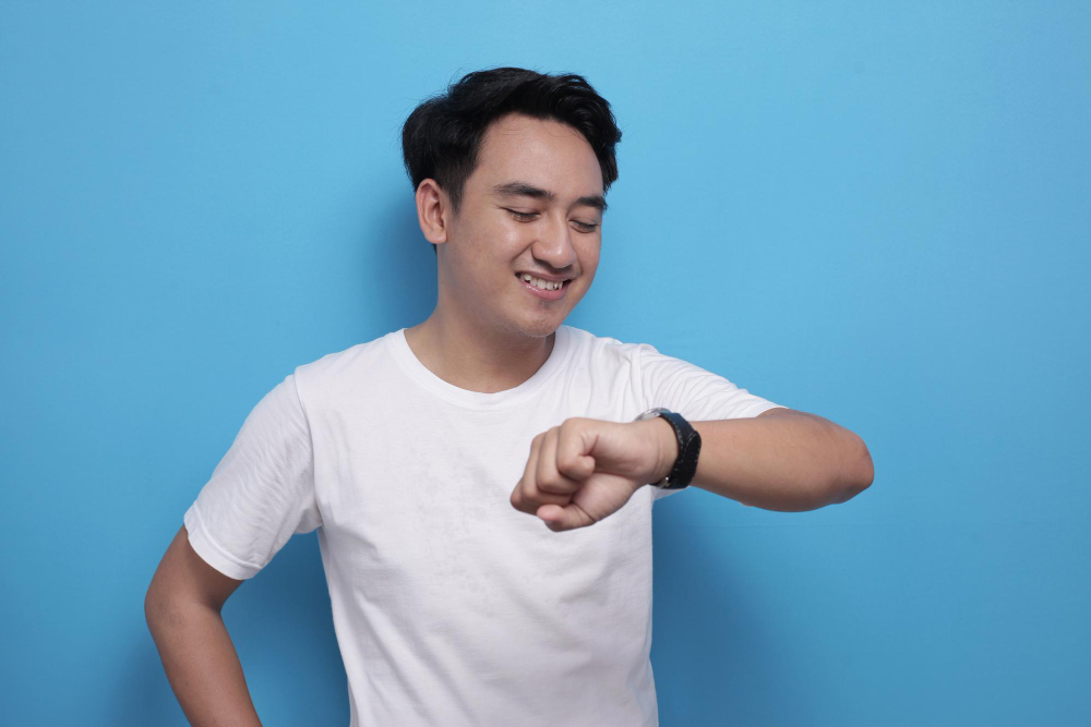 Man smiling, checking time on wristwatch, blue background.